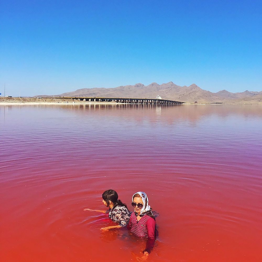 یک زن ایرانی همراه با دخترش در کنار بازمانده دریاچه ارومیه، یکی از بزرگ‌ترین دریاچه‌های شور جهان، در شمال غربی ایران . طیف قرمز به دلیل وجود نوعی از هالوباکتریاسی به نا هالوفیلس (نمک‌دوست) است که باکتری‌هایی هستند که در شرایط بسیار شور وجود دارند. این باکتری‌ها رنگ‌دانه‌های صورتی و قرمز تولید می‌کنند. وقتی تعداد آنها بسیار زیاد باشد می‌توانند رنگ آب را قرمز کنند. - مجید سعیدی</p>


<p>
