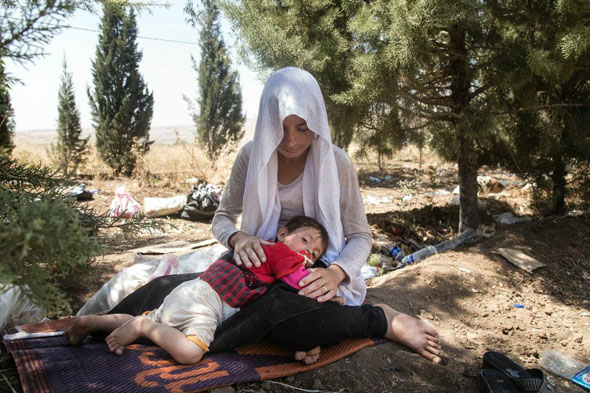 ویان اسماعیل، زن بیست ساله‌ی یزیدی سنجار پس از عبور از مرز سوریه همراه با پسر ۱۸ ماهه‌ی خود استراحت می‌کند. او ده روز را در کوه‌های سنجار بدون آب و غذا گذرانده است. عکس از: Zmnako Ismael/Metrography